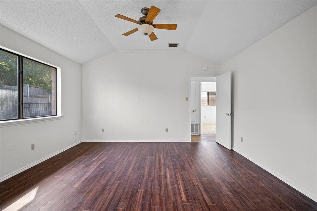 Vaulted ceiling featuring a central wood-blade ceiling fan with integrated light fixture, complemented by dark wood-finish flooring and a single-pane window