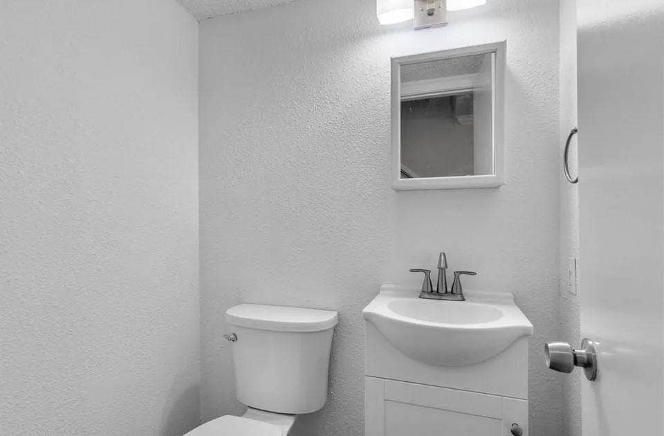 5326 Columbia Avenue, Dallas, TX 75214 A bright white half bathroom showcasing a toilet, a modern vanity with a simple mirror on the wall.
