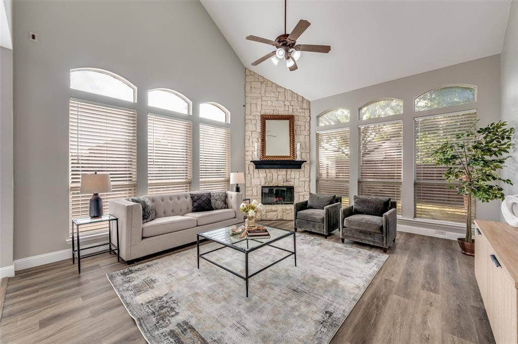 2873 Del Largo Way, Frisco, TX 75033 Vaulted ceiling, stone-clad fireplace, wood-finish flooring, multiple arched windows, and a ceiling fan with integrated lighting