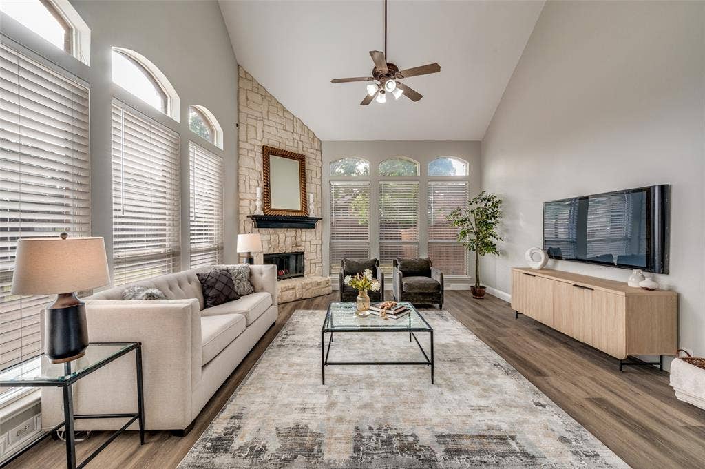 2873 Del Largo Way, Frisco, TX 75033 Vaulted ceiling with a ceiling fan, stone-clad fireplace with a mantel, multiple arched windows, and wood-finish flooring