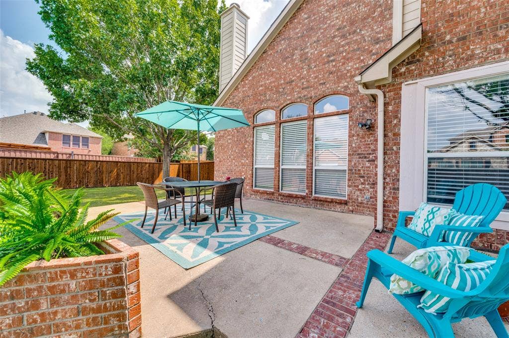 2873 Del Largo Way, Frisco, TX 75033 Expansive brick patio featuring mature landscaping, a built-in planter wall, and shaded seating area beneath a turquoise umbrella