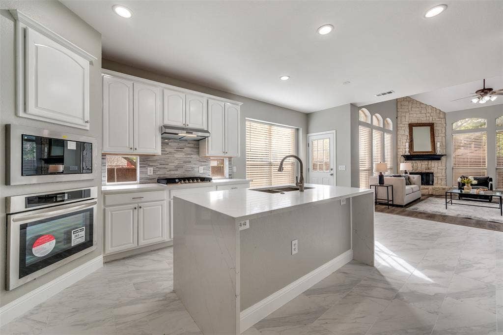2873 Del Largo Way, Frisco, TX 75033 Kitchen island with integrated sink, white cabinetry, integrated stainless steel appliances, and tile flooring