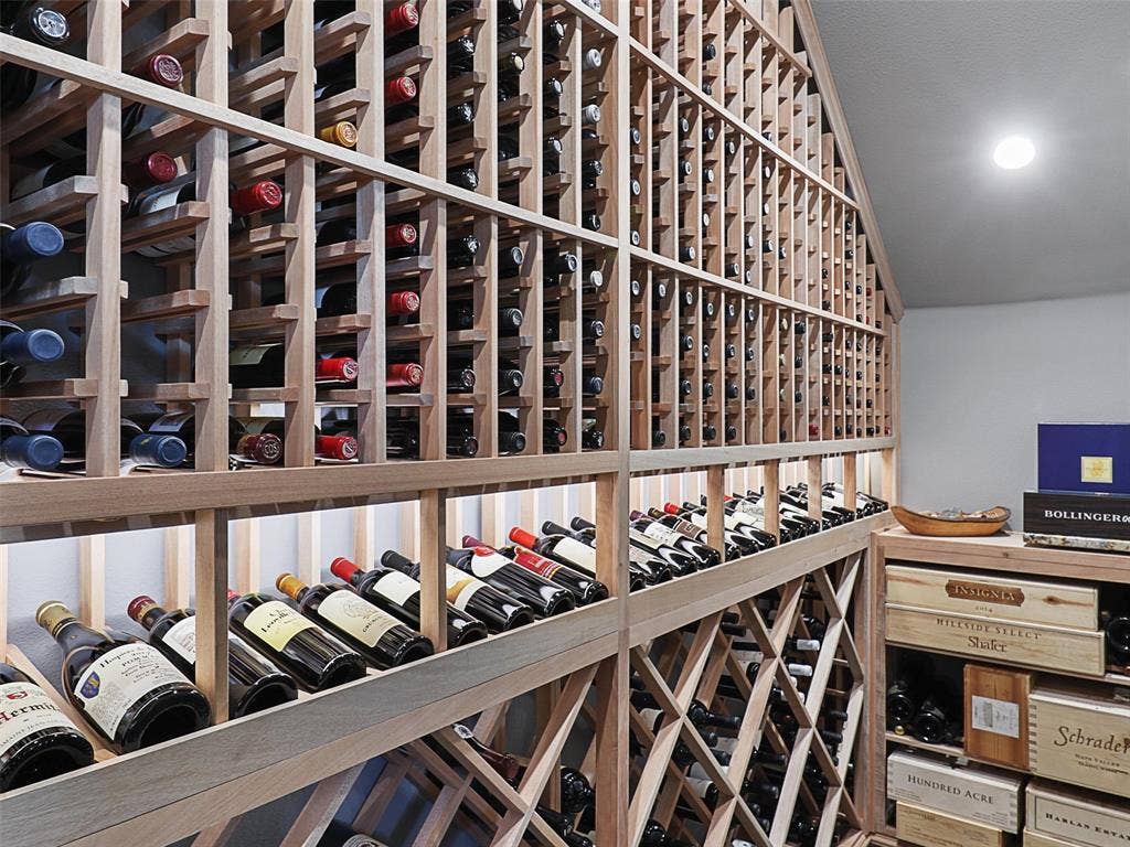 12921 Railhead Court, Frisco, TX 75033 One of the home's most distinctive features is its custom wine cellar, completed in 2022 and designed for the serious wine enthusiast. The cellar features a CellarPro 4000S split-system cooling unit engineered to regulate both temperature and humidity. Hard foam insulation within the walls and ceiling, along with moisture-resistant drywall, helps create a controlled environment for the collection. A custom iron entry door with UV-protective glass introduces the space, while custom solid mahogany racking accommodates standard 750ml bottles, larger champagne-style bottles, large-format bottles, and wood cases. Multiple lighting zones with dimmers create an elegant atmosphere, while storage capacity for approximately 800 bottles transforms the cellar into both a functional collection space and a striking architectural feature.