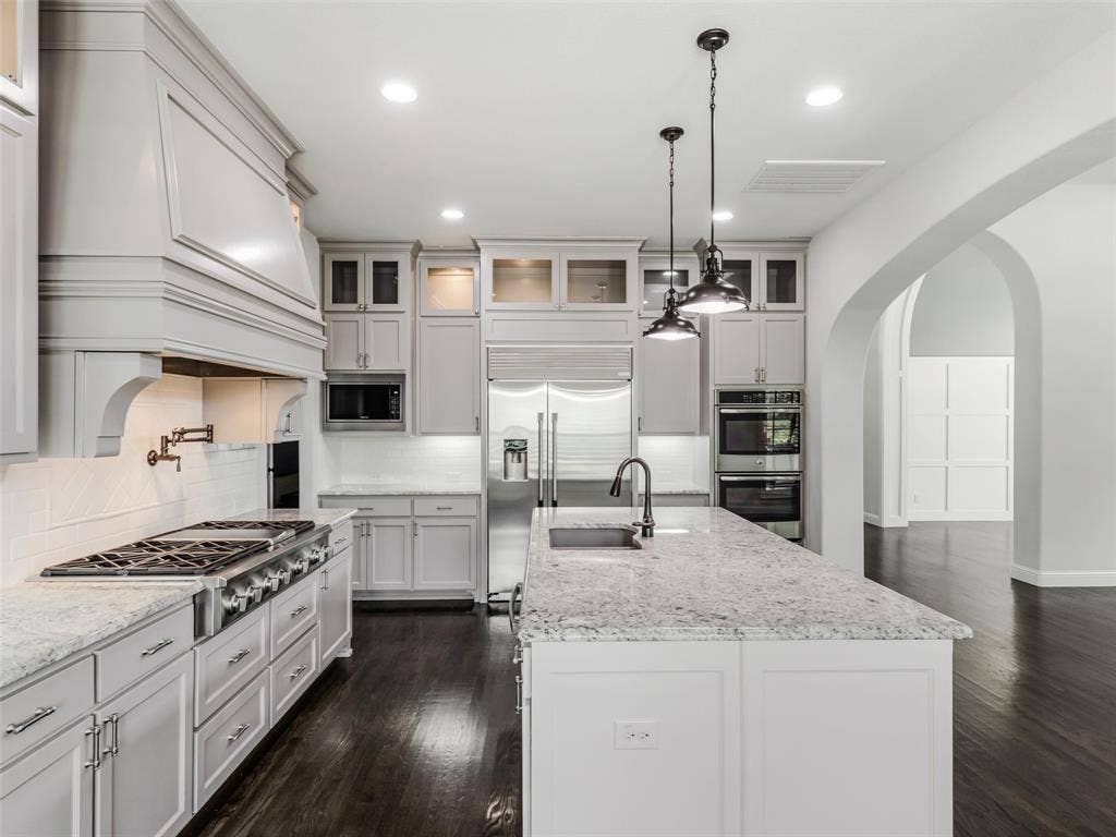 12921 Railhead Court, Frisco, TX 75033 At the heart of the home is a beautifully appointed kitchen featuring custom built-in cabinetry and an impressive collection of stainless-steel appliances. A commercial-grade gas cooktop with coordinating hood provides a centerpiece for the space, complemented by a built-in refrigerator, double ovens, built-in microwave, and a new dishwasher installed in 2025. The large center island offers breakfast bar seating and generous workspace, making the kitchen equally suited for everyday meals and entertaining.
