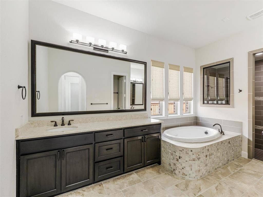 12921 Railhead Court, Frisco, TX 75033 The primary suite offers a spacious private retreat with an approximately 8-by-9-foot sitting area that can be used for reading, relaxing, or creating a quiet morning lounge. The generously sized ensuite bath measures approximately 11 by 18 feet and features a separate shower, soaking tub, and separate vanities with individual sinks. An approximately 10-by-14-foot walk-in closet provides extensive wardrobe storage and offers the added convenience of direct access to the laundry room, creating an efficient and thoughtfully planned connection between the spaces.