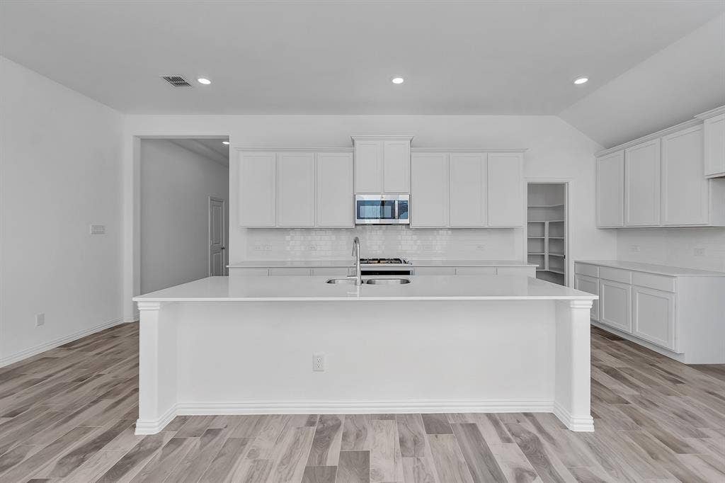 7204 Black Cherry Lane, McKinney, TX 75071 Kitchen with stainless steel microwave, a kitchen island with sink, decorative backsplash, light countertops, and lofted ceiling