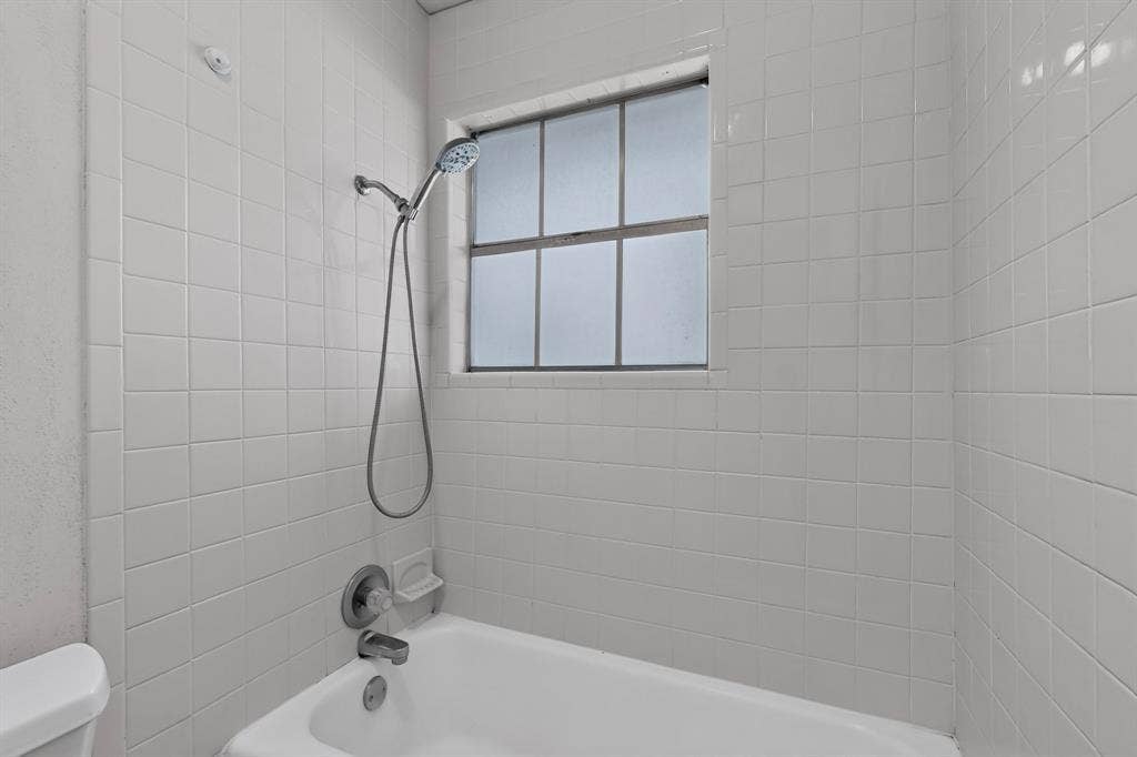 Tub and shower combination with white square tile surround, chrome fixtures, and a privacy window