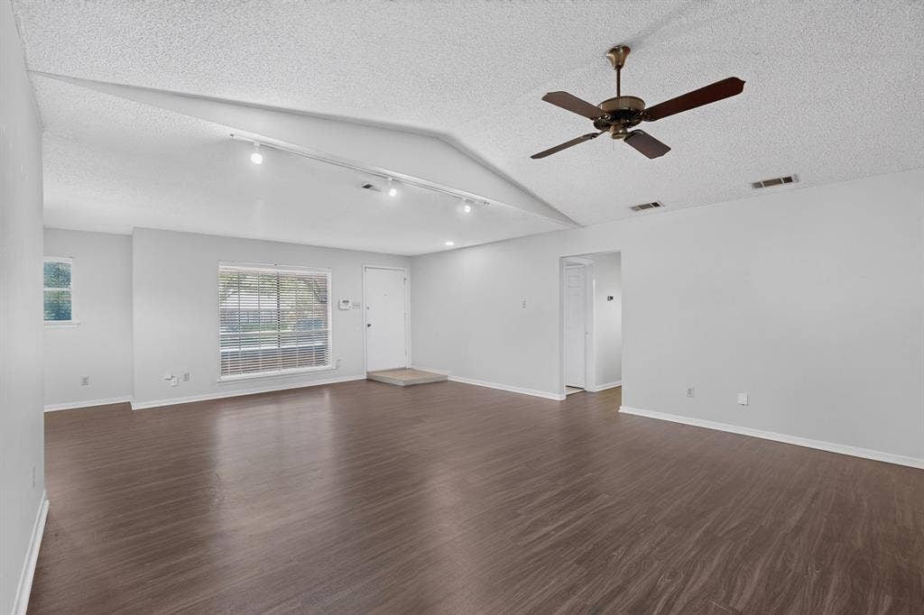 Vaulted ceiling featuring track lighting and a ceiling fan, wood-finish flooring, and a large front window