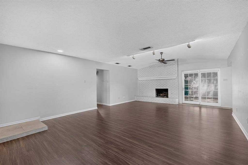 Vaulted ceiling with a ceiling fan, white brick fireplace, dark wood-finish flooring, recessed lighting, and sliding glass doors