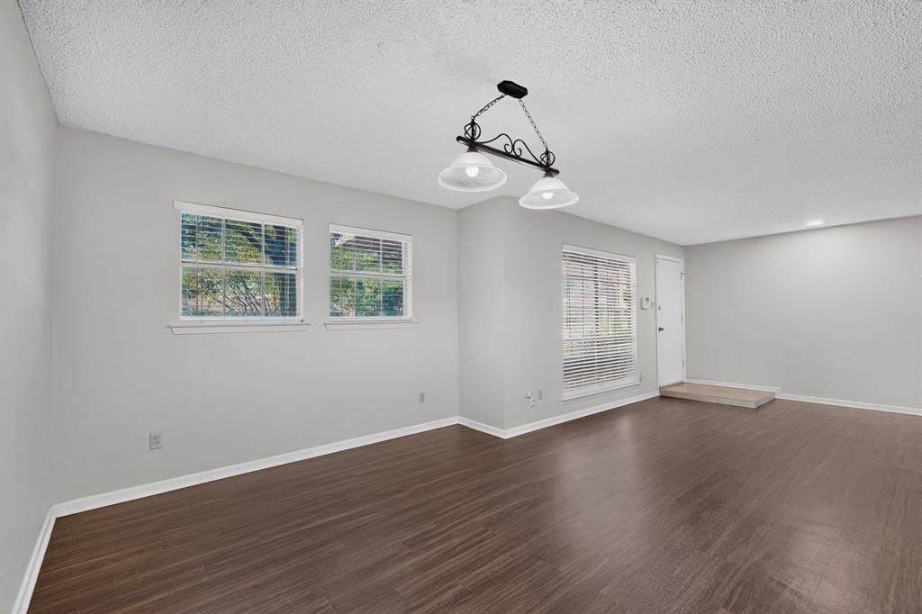 Wood-finish flooring, two large windows with blinds, recessed lighting, and a front entry door with a landing