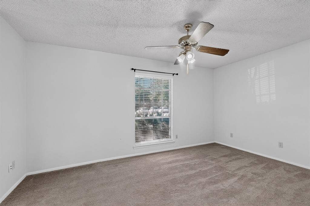 Spacious room featuring neutral carpeting, a single window with horizontal blinds, and a ceiling fan with integrated lighting
