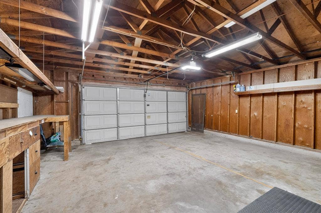 Attached garage with exposed wood ceiling beams, concrete flooring, and a built-in wood workbench