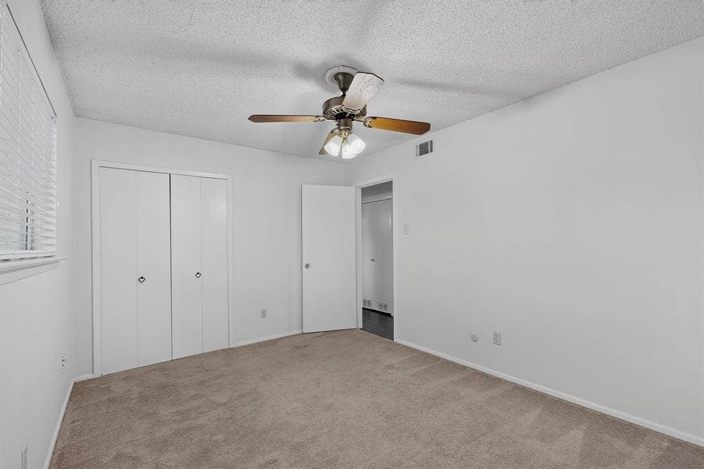 Neutral wall color, carpeted flooring, window with blinds, bi-fold closet doors, and a ceiling fan with integrated lighting