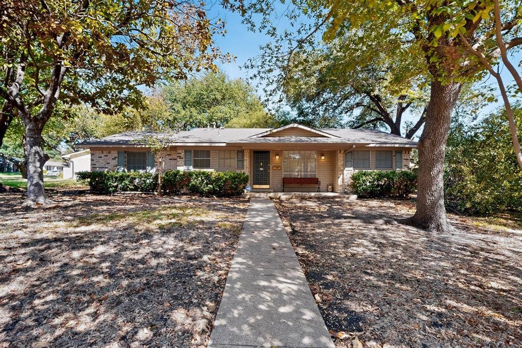 Brick and siding exterior with a front walkway, mature trees, and established landscaping