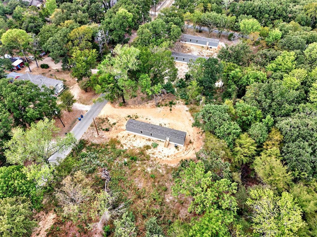 Aerial perspective of a detached single-story residence situated on a lot featuring mature tree coverage and paved road access