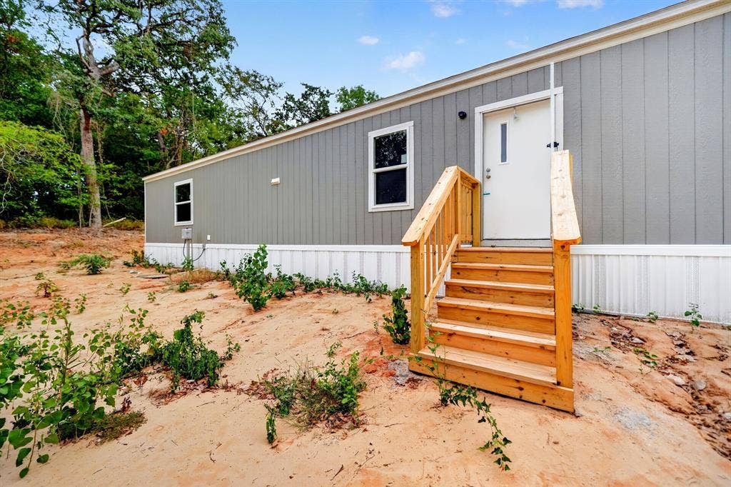 Exterior featuring vertical grey siding, white skirting, double-pane windows, and a wood staircase with matching handrails