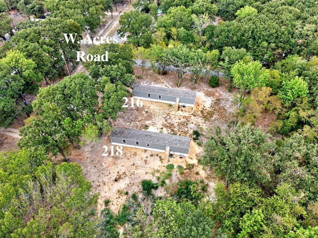 Aerial perspective of two structures featuring shingled roofs and gray siding, situated on a lot surrounded by mature trees