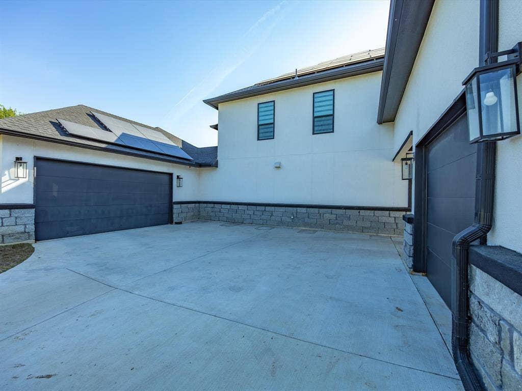 View of side of property featuring roof mounted solar panels, a garage, stucco siding, and driveway