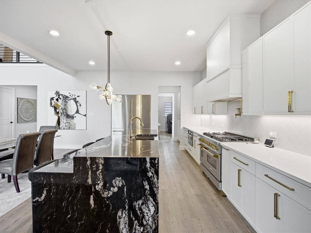 Kitchen featuring white cabinetry, high quality appliances, light wood-style flooring, and light stone counters