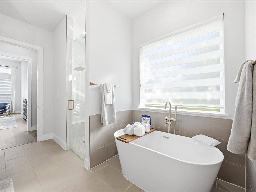 Full bathroom featuring a shower stall, a soaking tub, healthy amount of natural light, light tile patterned flooring, and tile walls