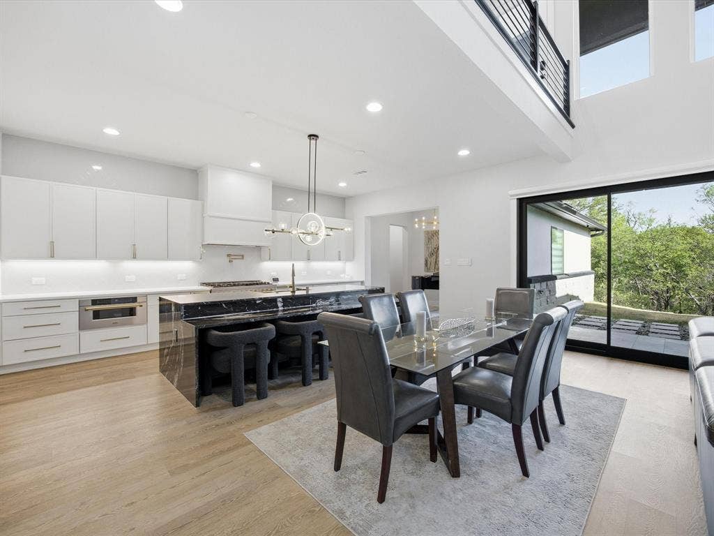 Dining area with suspended lighting, light wood-style floors, and a high ceiling