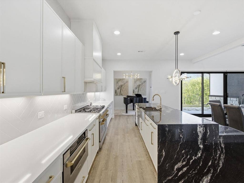 Kitchen featuring white cabinetry, stainless steel appliances, light wood-style floors, an island with sink, and dark stone countertops