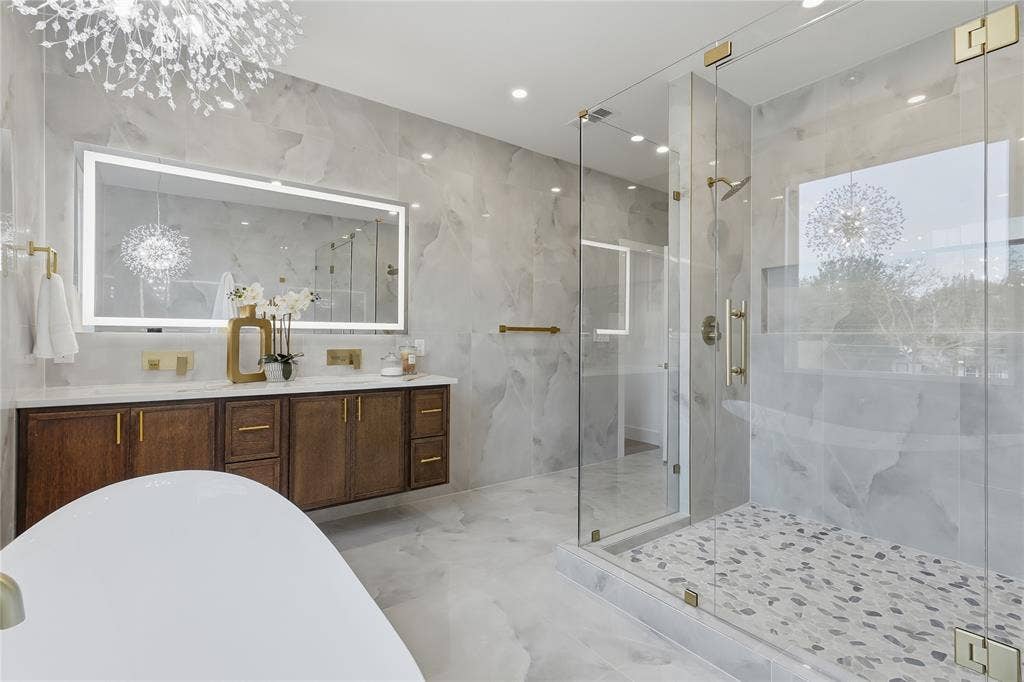 3424 Navaro Street, Dallas, TX 75212 Freestanding soaking tub, dual vanity with wood cabinetry, backlit mirror, glass-enclosed shower with pebble-style floor, and ceiling-mounted light fixture