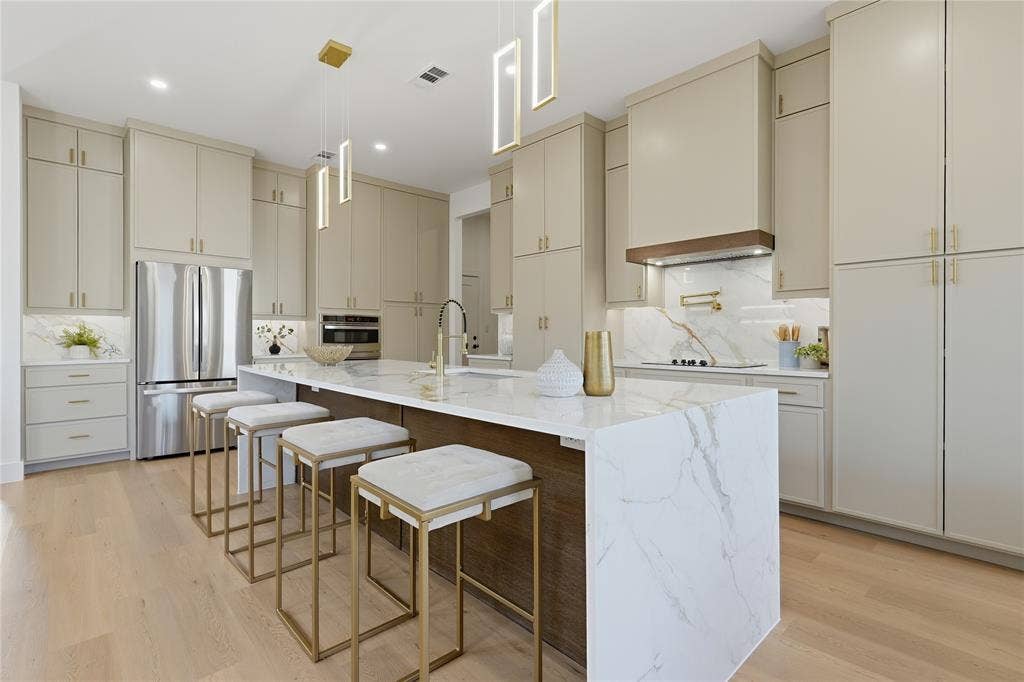3424 Navaro Street, Dallas, TX 75212 Kitchen featuring light wood-finish flooring, a waterfall island with stone countertop, stainless steel appliances, pendant lighting, and abundant cabinetry