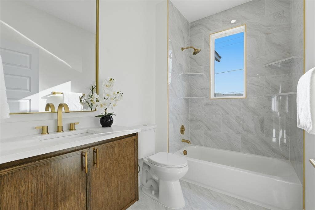 3424 Navaro Street, Dallas, TX 75212 Bathroom with a wood-finish vanity, white countertop, gold-tone fixtures, and a white bathtub with tile surround