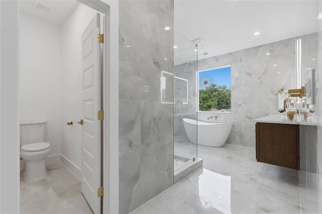 3424 Navaro Street, Dallas, TX 75212 Floating vanity with a light-colored countertop, freestanding soaking tub, large window, and wall-mounted plumbing fixtures