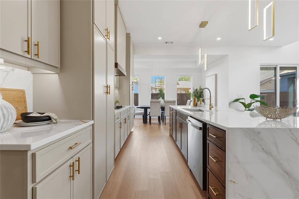 3424 Navaro Street, Dallas, TX 75212 Gourmet kitchen featuring a large waterfall island with integrated sink, two-tone cabinetry, wood-finish flooring, and contemporary pendant lighting