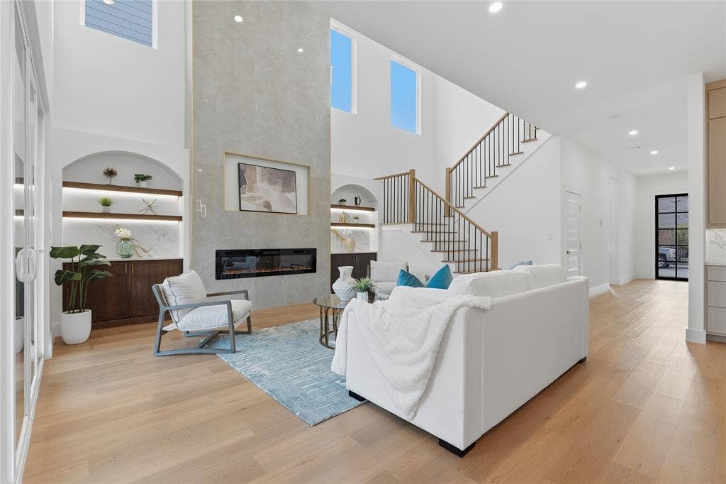 3424 Navaro Street, Dallas, TX 75212 Two-story living area with wood-finish flooring, a linear fireplace set in a stone-look accent wall, and built-in shelving with integrated lighting