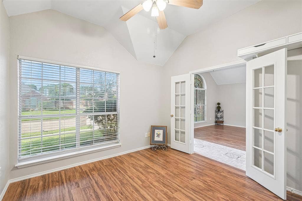 Vaulted ceiling, wood-finish flooring, large window with blinds, French doors, and a ceiling fan