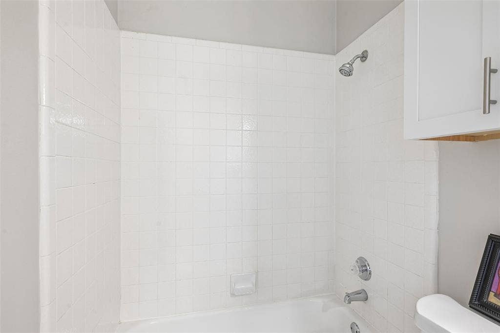 Tub and shower combination featuring white square tile surround, chrome showerhead, and chrome tub filler