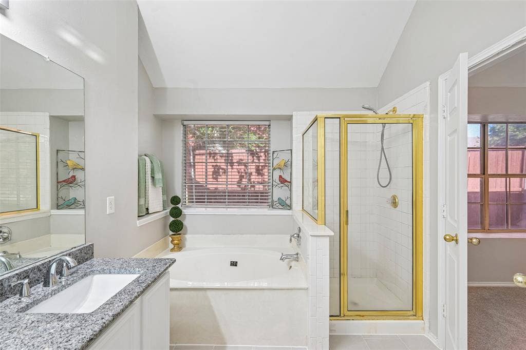 Built-in soaking tub, walk-in shower with gold-finish frame, single vanity with granite-style countertop, and integrated sink