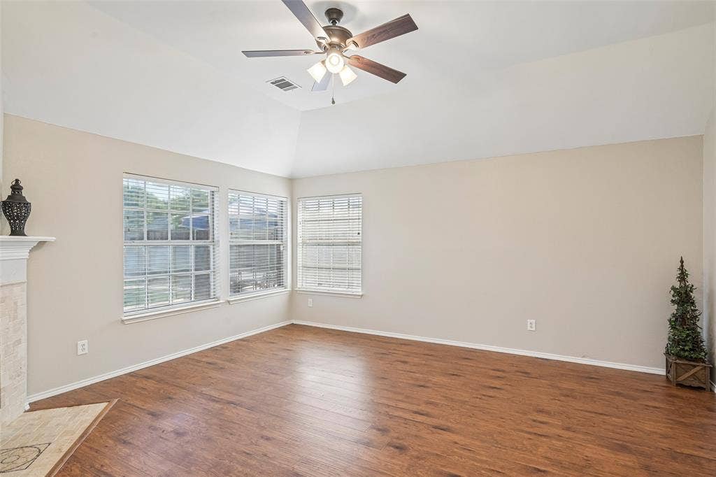 Vaulted ceiling with an integrated ceiling fan, wood-finish flooring, multiple windows with blinds, and a tiled fireplace surround