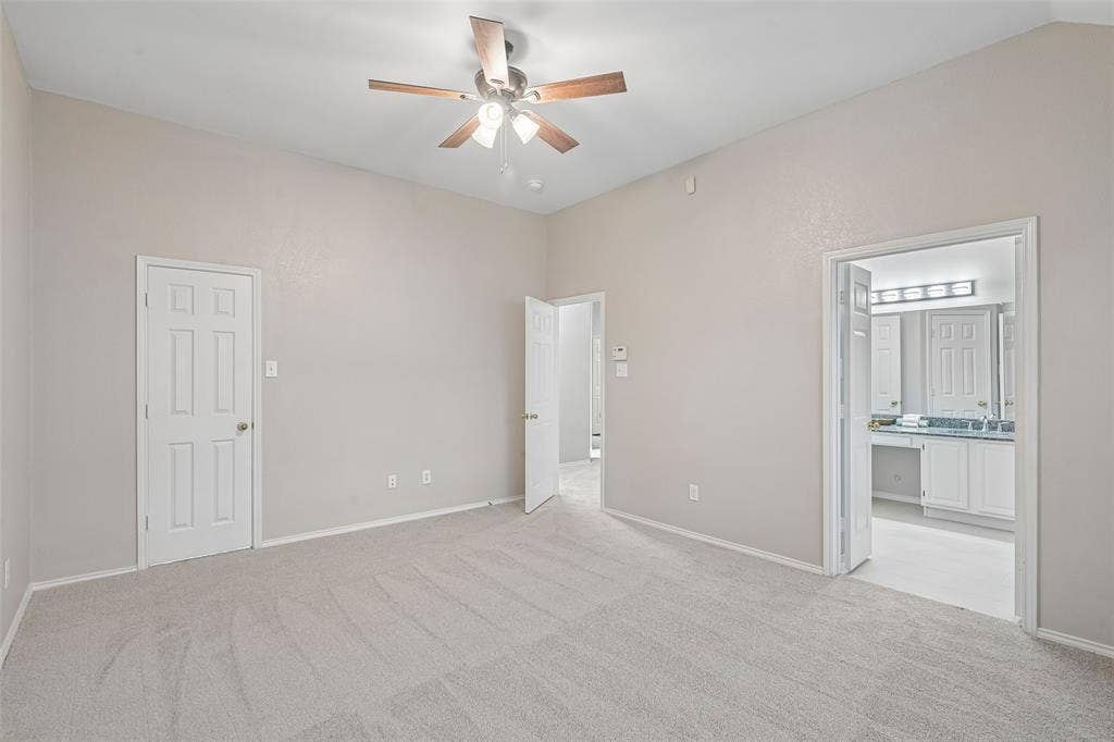 New Carpeted flooring, vaulted ceiling, ceiling fan with light fixture, white paneled doors, and an open doorway to an adjacent room
