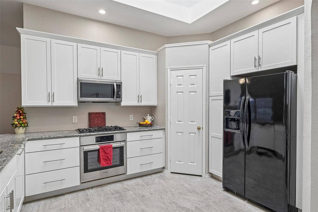 Modern kitchen featuring white shaker-style cabinetry with chrome hardware, stainless steel appliances including a gas range and black French-door refrigerator, granite countertops, recessed lighting, and neutral tile flooring throughout