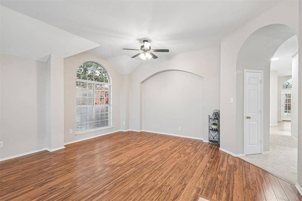 Spacious living area showcasing warm wood-finish flooring, soaring ceilings with curved architectural details, and a ceiling fan with brushed metal finish