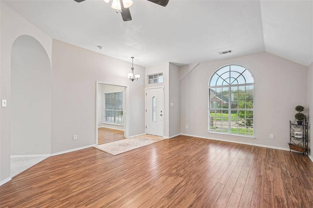 Spacious living area featuring gleaming laminate flooring, vaulted ceilings with ceiling fan, and an arched transom window framing natural light