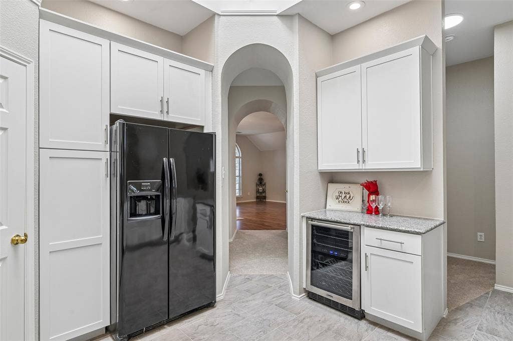 Refrigerator with ice and water dispenser, white shaker-style cabinetry, granite-finish countertop, and integrated beverage cooler