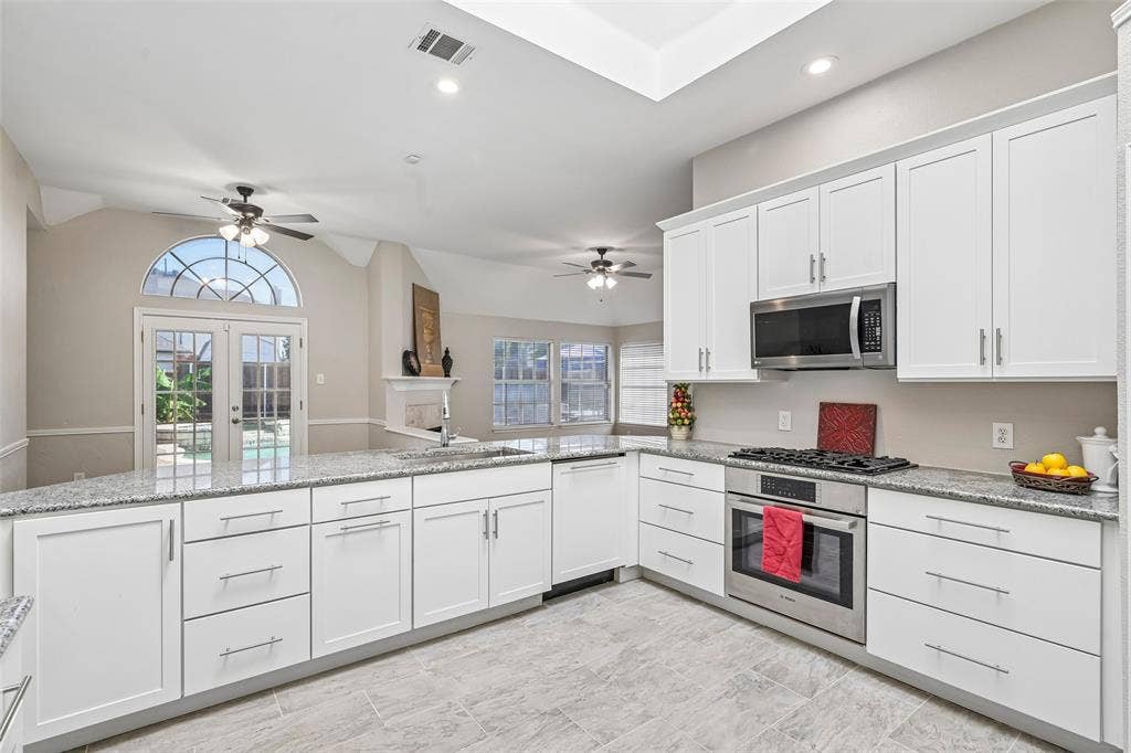 Kitchen featuring white shaker cabinetry, granite countertops, tile flooring, stainless steel appliances, and a vaulted ceiling with recessed lighting