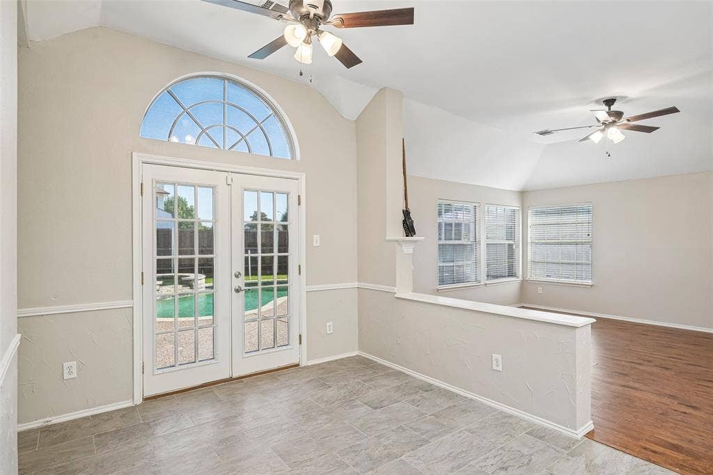 Arched transom window above French doors, vaulted ceiling, tile flooring, wood-finish flooring, two ceiling fans with light fixtures