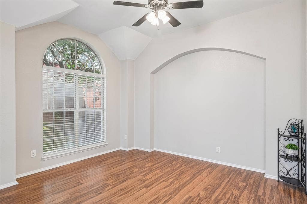 Arched window with blinds, vaulted ceiling, ceiling fan, and an arched wall niche