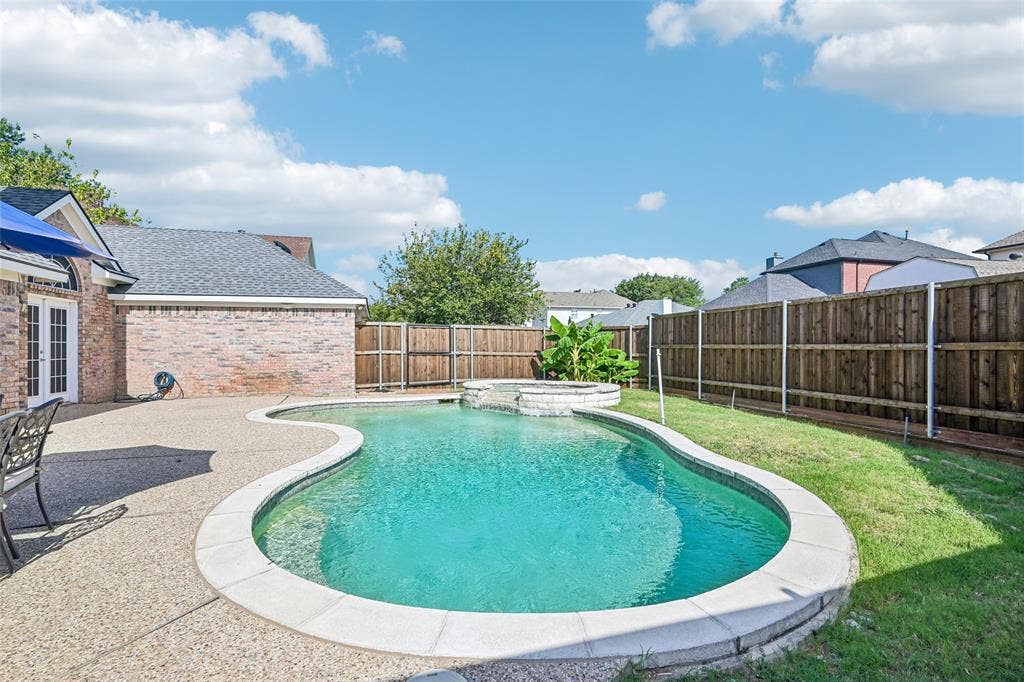 Curved swimming pool with an integrated spa, surrounded by a concrete patio and a landscaped lawn