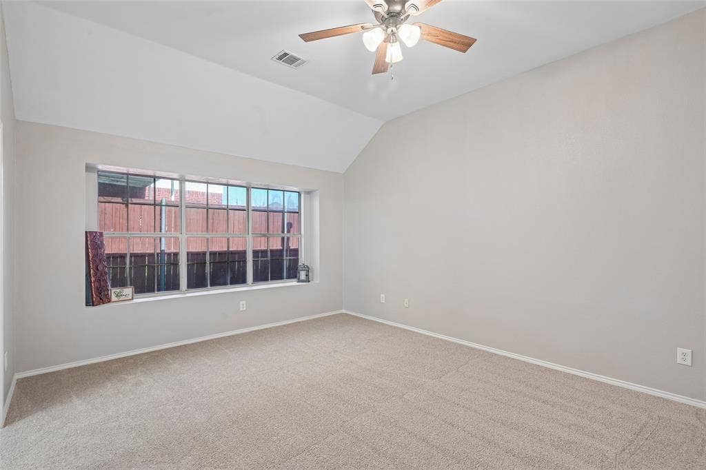 Vaulted ceiling, ceiling fan with light fixture, neutral-tone carpeting, large window with deep sill, light gray wall finishes