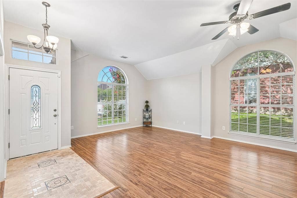 Laminate flooring, vaulted ceilings, and arched windows with blinds