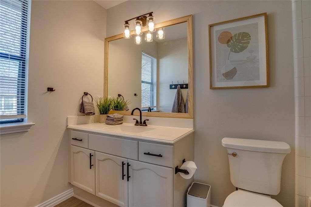 6003 Lloyd Court, Dallas, TX 75252 Vanity with white cabinetry, countertop, and an integrated sink, featuring a wood-framed mirror with a four-bulb light fixture