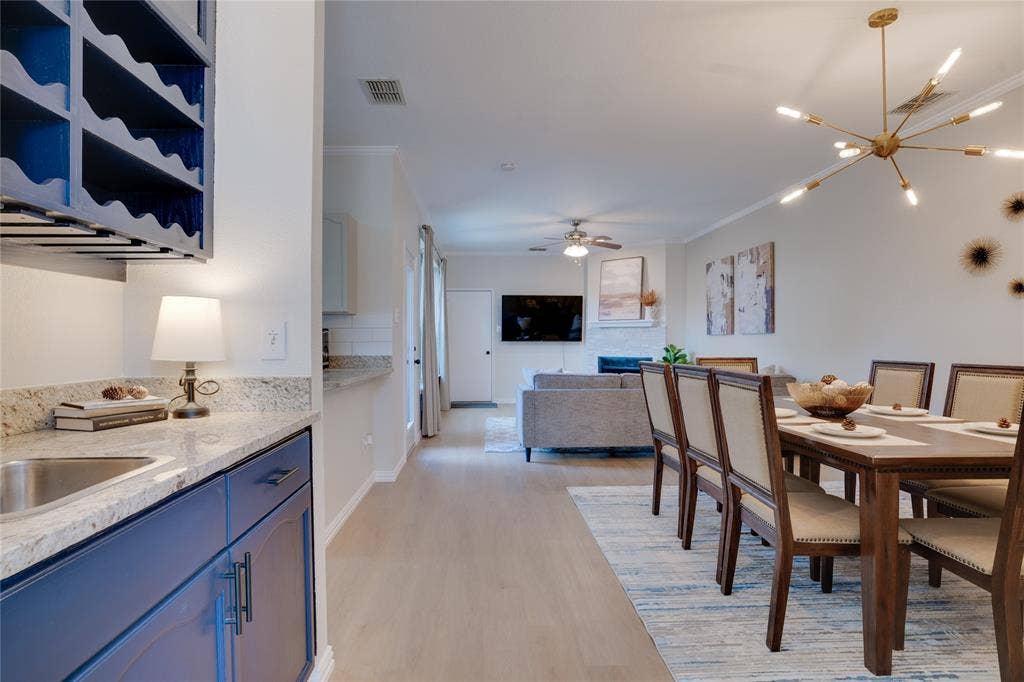 6003 Lloyd Court, Dallas, TX 75252 Open-concept living space featuring wood-finish flooring, a contemporary chandelier, and a built-in wet bar with blue cabinetry and a stainless steel sink