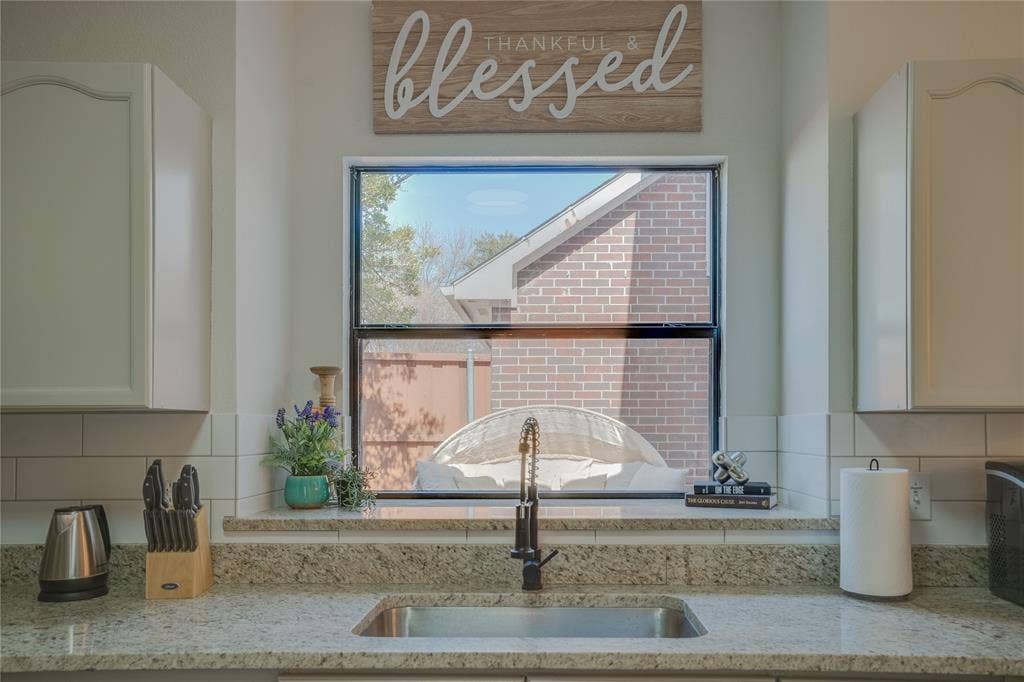 6003 Lloyd Court, Dallas, TX 75252 Stainless steel sink with a matte black faucet, light granite countertops, white subway tile backsplash, and white upper cabinetry